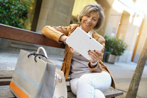 Older woman on bench with tablet and shopping bags